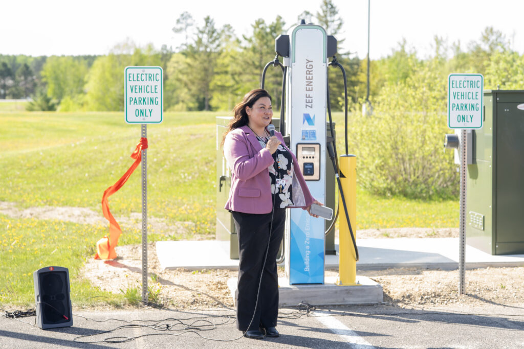 Woman speaking with a microphone in front of an EV charger.